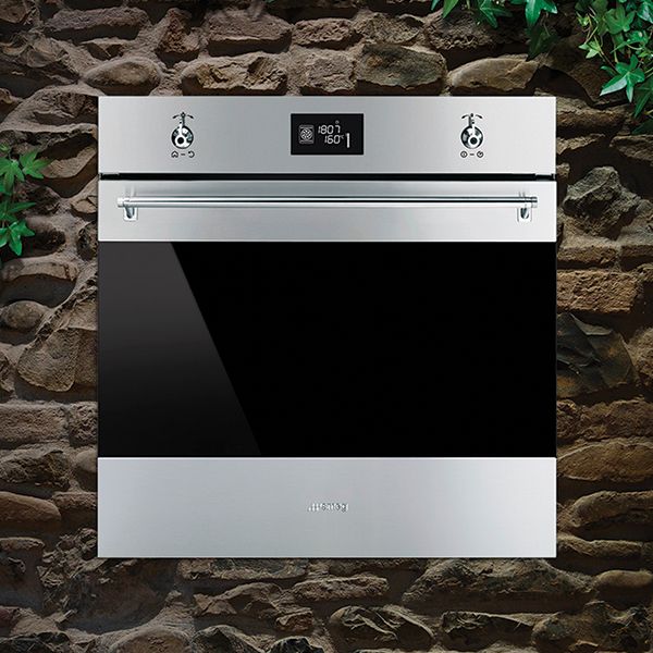 A class range of appliances (shown, is a built-in oven from the range) in stainless steel, with chrome handle and control dials, black glass, and a centralised control panel.