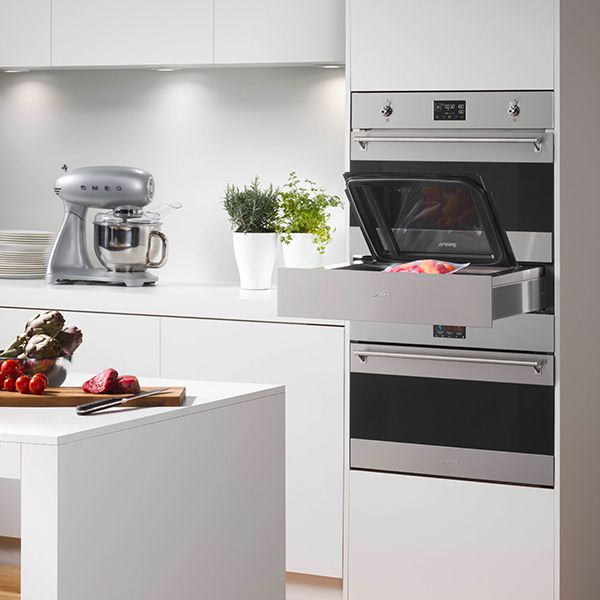 A stainless steel built-in chiller unit underneath a built-in oven. The drawer is open showing a top opening lid and vacuum packed food inside