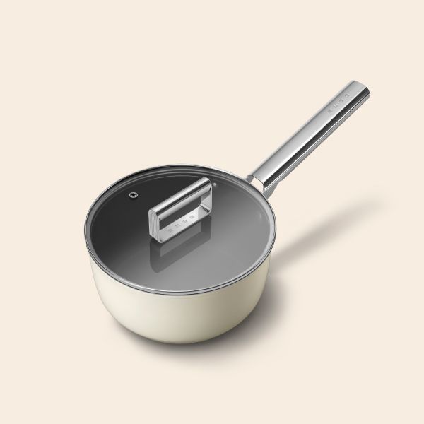 A non-stick cream saucepan with a long stainless steel handle. On top sits a glass lid with a stainless steel handle