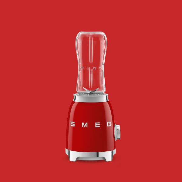 A bright red personal blender in Smeg's iconic retro design, featuring chrome highlights and a slim, clear blender container